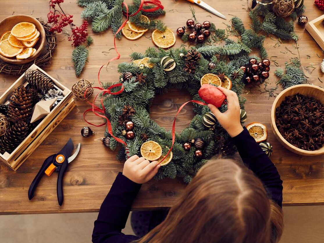 High angle view of busy woman standing at desk and using decorative ribbon while making Christmas wreath